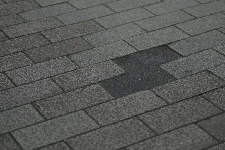 A homeowner examines curled and cracked asphalt shingles from the ground beside a residential roof.